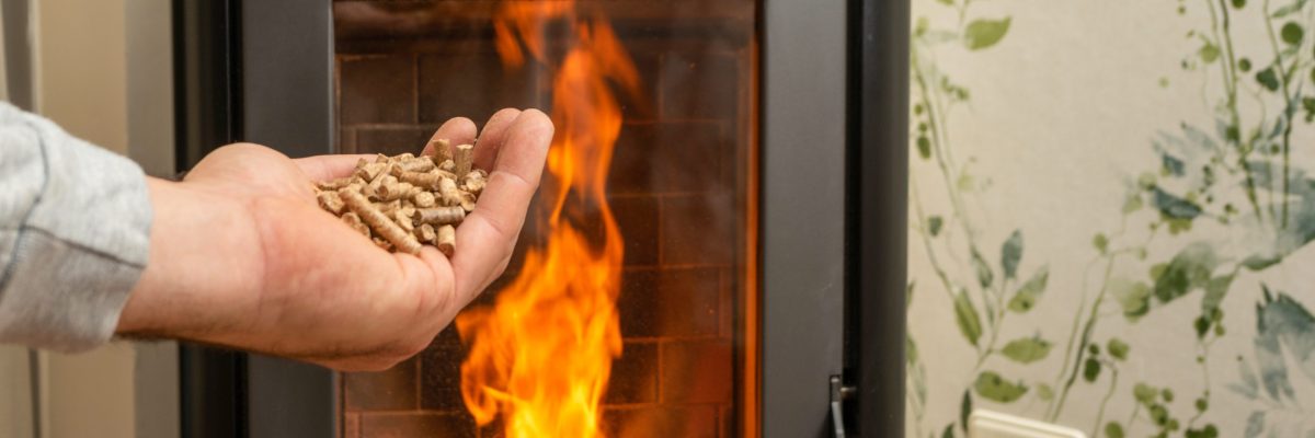 Ofen mit Feuer im Hintergrund, Hand mit Pellets im Vordergrund