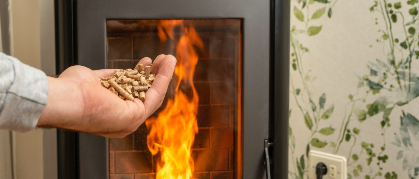 Ofen mit Feuer im Hintergrund, Hand mit Pellets im Vordergrund