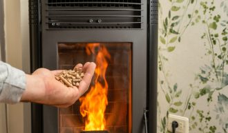 Ofen mit Feuer im Hintergrund, Hand mit Pellets im Vordergrund