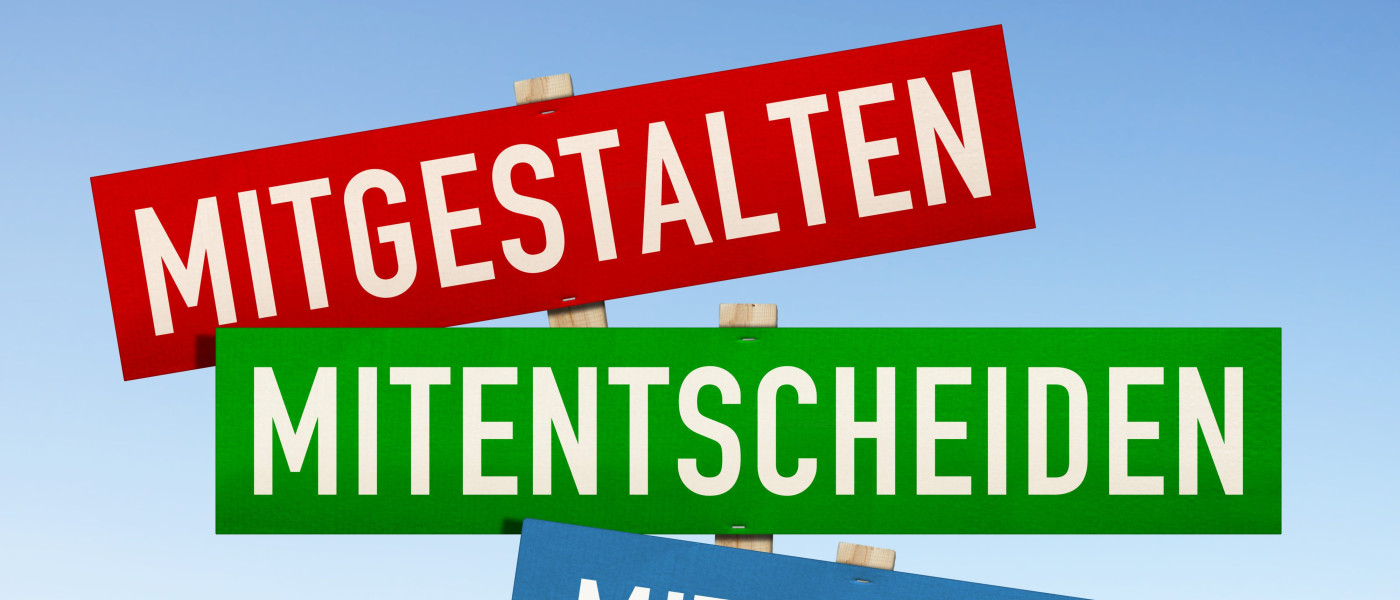 Dieses Bild zeigt den Schriftzug Mitgestalten, Mitentscheiden und Mitdenken auf einem roten, grünen und blauen Schild